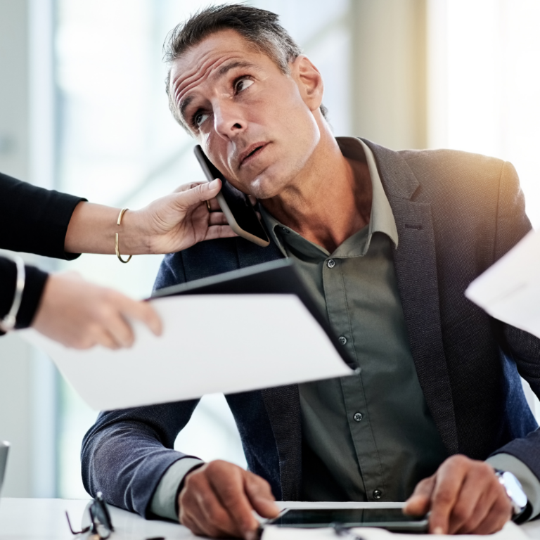 over worked man on phone with arms shoving paperwork representing a b2b buyer