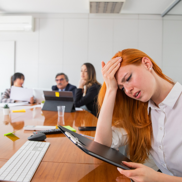 Gen Z-aged woman with long red hair looking stressfully down at tablet during a sales meeting as she is in the trenches of sales enablement